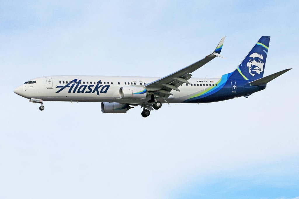 Alaska Airlines aircraft flying against a clear sky, displaying aviation and travel concepts.
